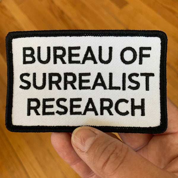 Iron-on patch with text: BUREAU OF SURREALIST RESEARCH in black lettering on white background with a black border